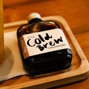 Botella de vidrio oscuro con etiqueta de cold brew sobre una bandeja de madera