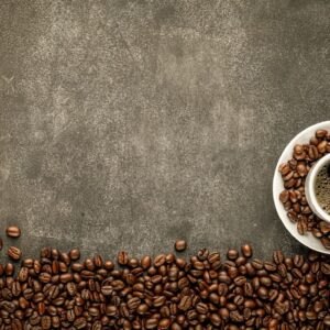 Taza de café sobre un plato rodeada de granos de café tostado sobre un fondo gris oscuro
