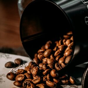 Granos de café tostado derramándose de un recipiente oscuro sobre una mesa