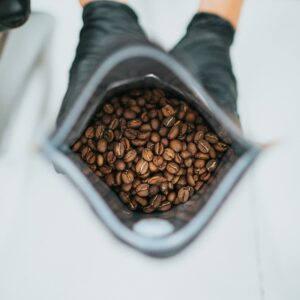 Manos con guantes negros sosteniendo una bolsa abierta llena de granos de café tostado