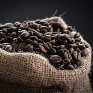 Saco de yute lleno de granos de café de tostión oscura sobre fondo negro