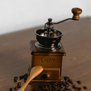 Molinillo manual de madera con manivela, cuchara de madera y granos de café esparcidos