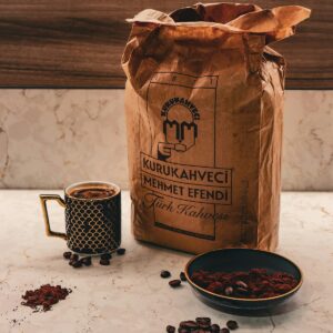 Bolsa de papel de café junto a una taza y un cuenco con granos tostados sobre una mesa de mármol