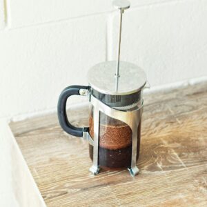 Prensa francesa de vidrio y acero con café sobre una repisa de madera clara