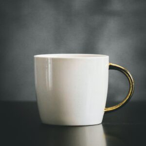 Taza blanca de cerámica con asa dorada sobre un fondo oscuro
